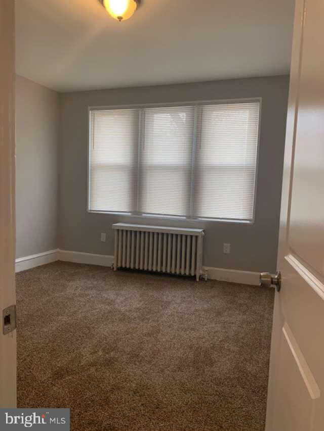 unfurnished room with radiator heating unit and carpet