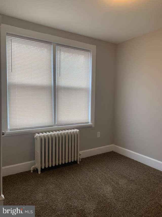 empty room featuring radiator heating unit and carpet