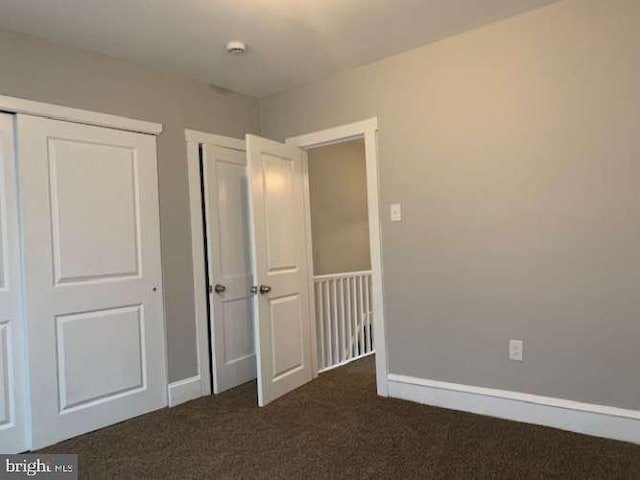 unfurnished bedroom with dark carpet and a closet