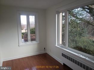 unfurnished room featuring dark wood-type flooring, radiator heating unit, and plenty of natural light