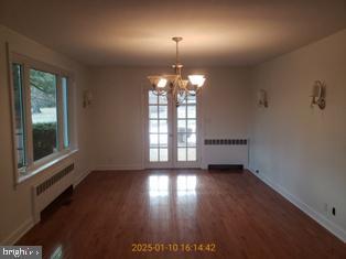 unfurnished dining area with dark hardwood / wood-style flooring, radiator, and a notable chandelier