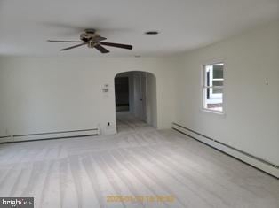 empty room with light colored carpet, ceiling fan, and baseboard heating