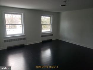 empty room featuring dark wood-type flooring and radiator heating unit