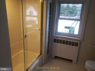 bathroom with radiator heating unit, enclosed tub / shower combo, and toilet