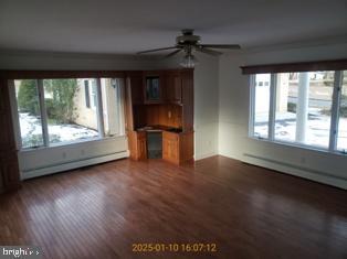 unfurnished living room with ceiling fan, dark hardwood / wood-style floors, and a baseboard heating unit