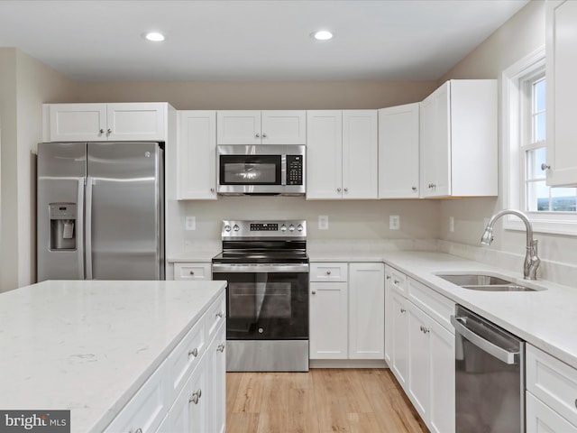 kitchen with light stone countertops, appliances with stainless steel finishes, light wood-type flooring, sink, and white cabinets