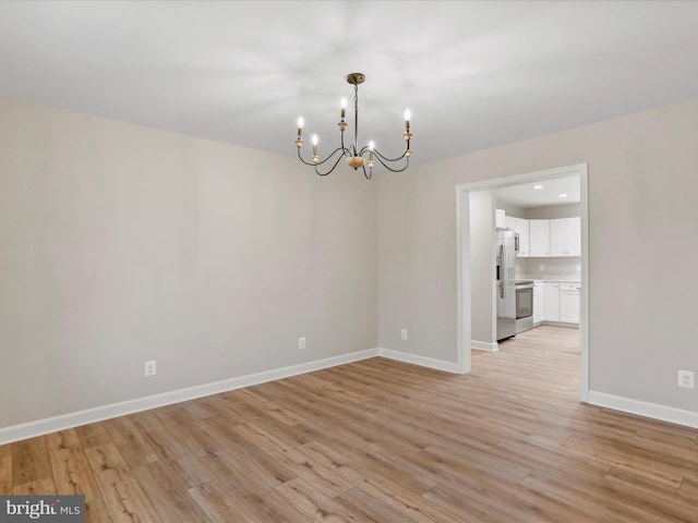 spare room featuring light wood-type flooring and a notable chandelier