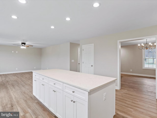 kitchen with light stone counters, ceiling fan with notable chandelier, decorative light fixtures, white cabinets, and light hardwood / wood-style floors