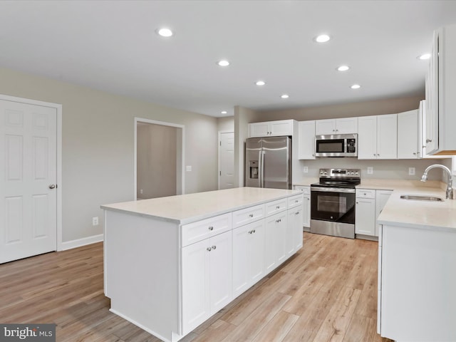 kitchen featuring appliances with stainless steel finishes, sink, light hardwood / wood-style flooring, white cabinets, and a center island