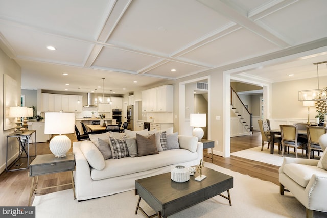 living room featuring beamed ceiling, light hardwood / wood-style floors, an inviting chandelier, and coffered ceiling