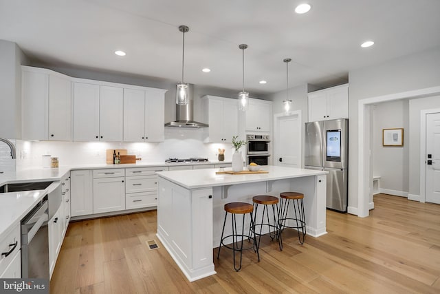 kitchen featuring white cabinets, light wood-type flooring, wall chimney range hood, and appliances with stainless steel finishes