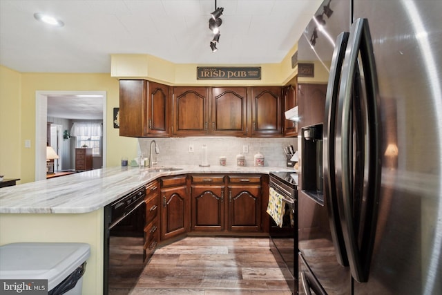 kitchen with kitchen peninsula, tasteful backsplash, sink, black appliances, and light hardwood / wood-style flooring