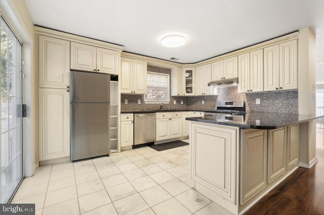 kitchen with tasteful backsplash, kitchen peninsula, cream cabinets, and appliances with stainless steel finishes