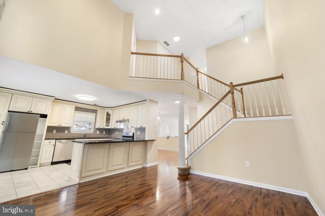 kitchen featuring backsplash, high vaulted ceiling, light hardwood / wood-style flooring, appliances with stainless steel finishes, and cream cabinetry