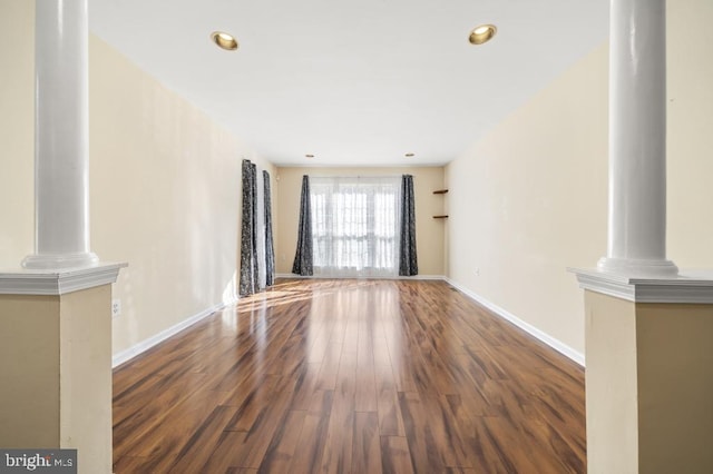 unfurnished living room featuring decorative columns and dark hardwood / wood-style floors