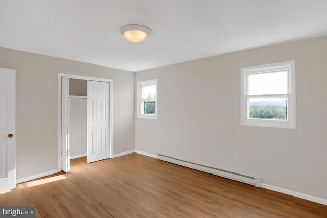 unfurnished bedroom with a closet, a baseboard radiator, and wood-type flooring