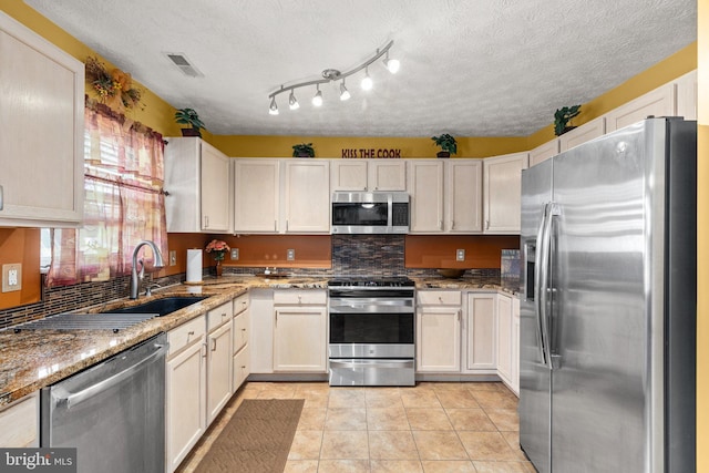 kitchen featuring sink, light stone countertops, a textured ceiling, light tile patterned flooring, and stainless steel appliances