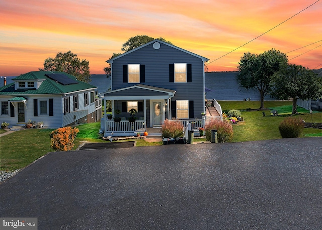 view of front facade with solar panels, covered porch, and a yard