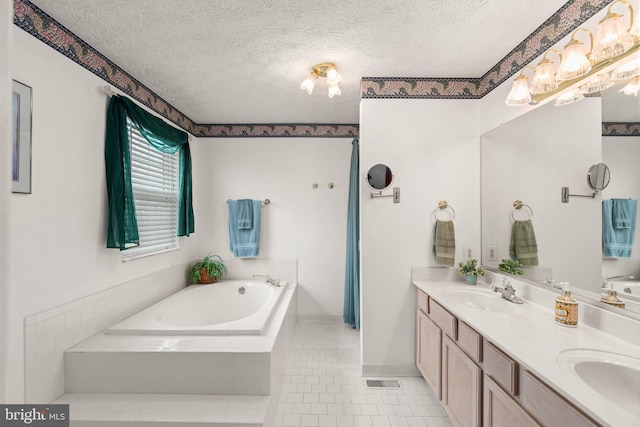 bathroom featuring tile patterned floors, tiled bath, vanity, and a textured ceiling