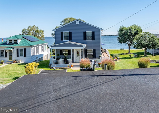 view of front facade with solar panels, a porch, a water view, and a front lawn