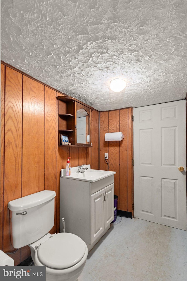 bathroom with vanity, wooden walls, toilet, a textured ceiling, and concrete flooring