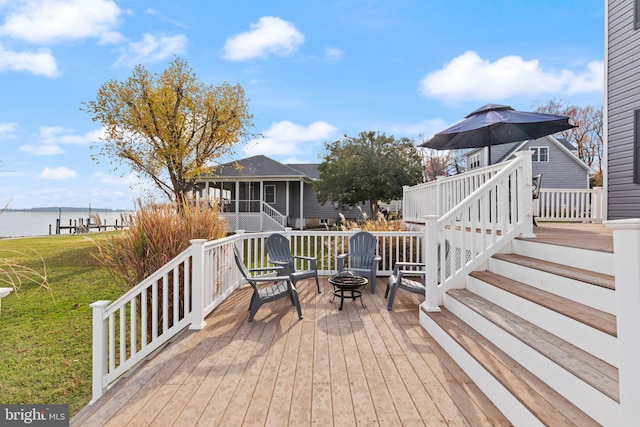 deck featuring a lawn, a sunroom, a water view, and a fire pit