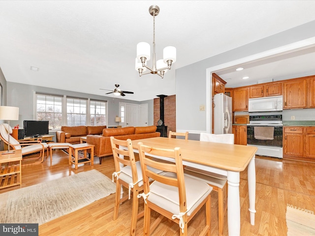 dining room featuring ceiling fan with notable chandelier, light hardwood / wood-style floors, and a wood stove