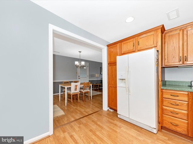 kitchen featuring white refrigerator with ice dispenser, pendant lighting, light wood-type flooring, and an inviting chandelier