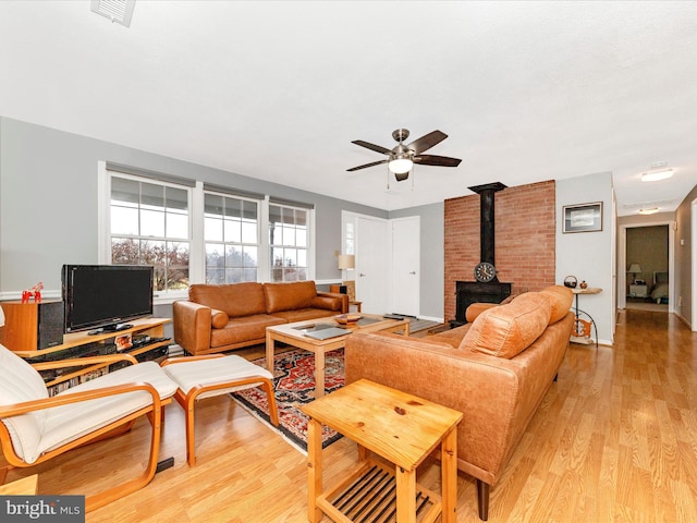 living room featuring a wood stove, ceiling fan, and light hardwood / wood-style floors