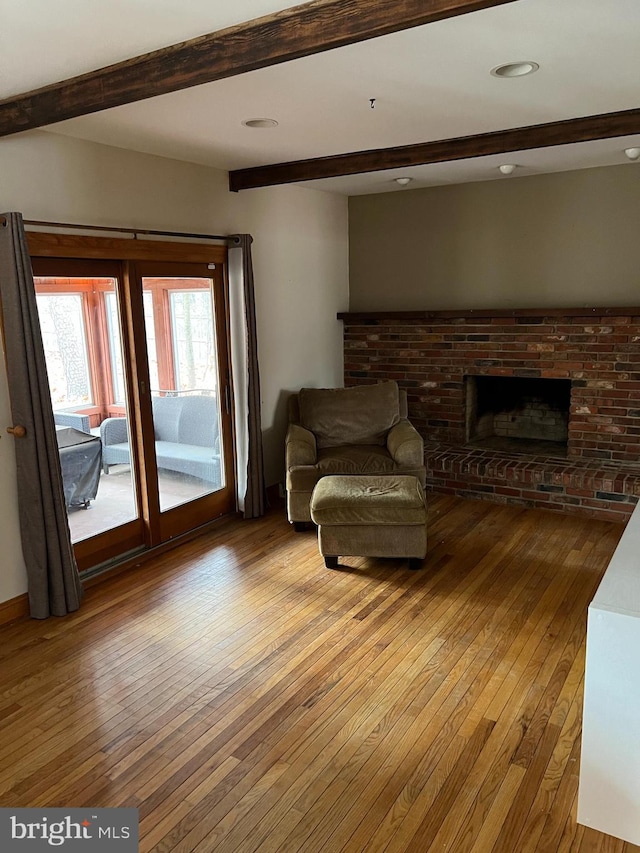 living room featuring beamed ceiling, light wood-type flooring, and a brick fireplace