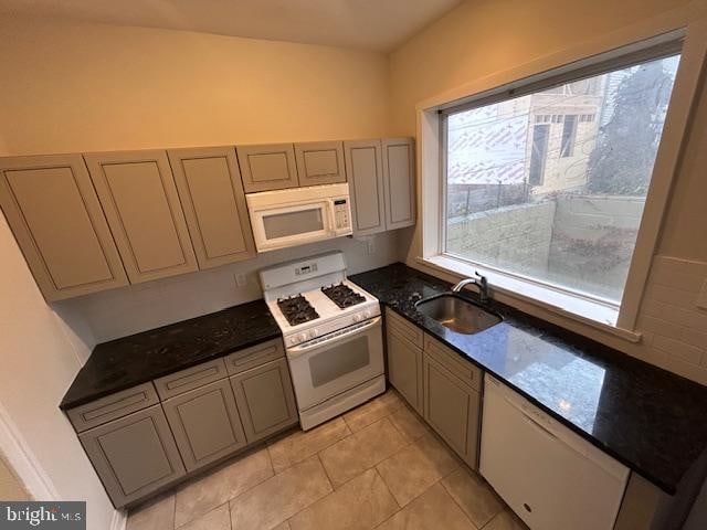 kitchen featuring white appliances, sink, light tile patterned flooring, dark stone counters, and gray cabinets