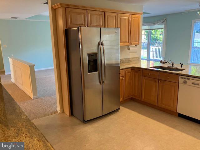 kitchen with white dishwasher, sink, stainless steel refrigerator with ice dispenser, light colored carpet, and kitchen peninsula