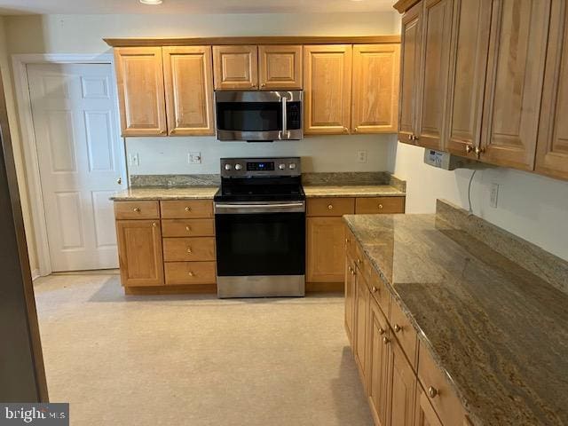 kitchen featuring light colored carpet, stainless steel appliances, and dark stone counters