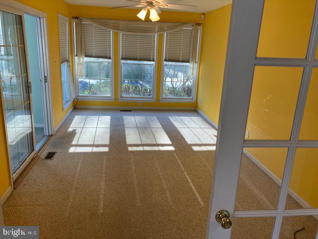 unfurnished room featuring light carpet, a wealth of natural light, and ceiling fan