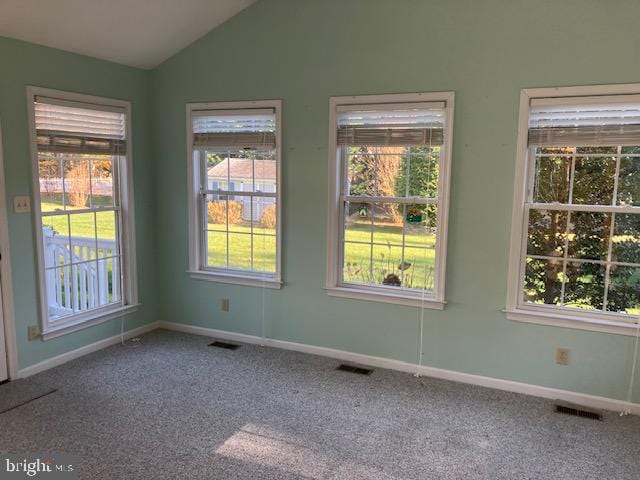 carpeted empty room featuring a wealth of natural light and lofted ceiling