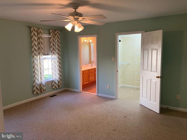 unfurnished bedroom featuring light carpet, a walk in closet, ensuite bathroom, and ceiling fan