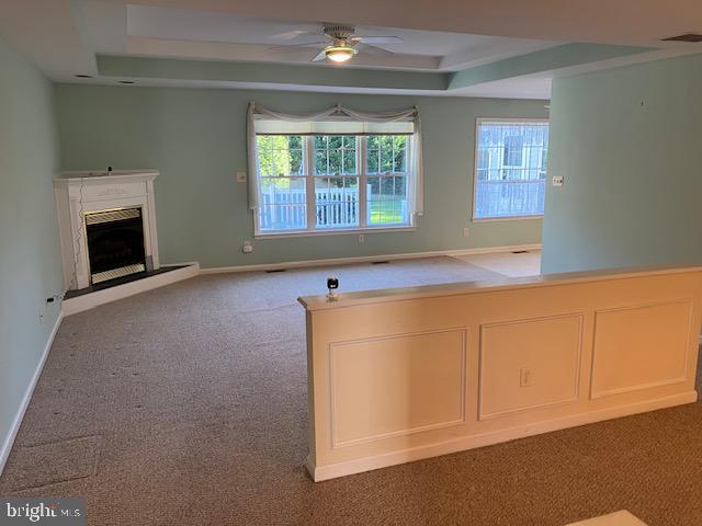 unfurnished living room featuring carpet flooring, ceiling fan, a healthy amount of sunlight, and a premium fireplace