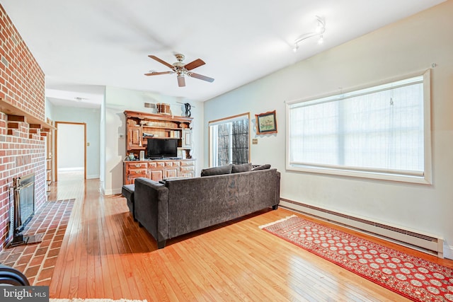 living room featuring ceiling fan, wood-type flooring, baseboard heating, and a brick fireplace