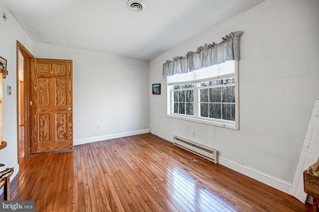 empty room with wood-type flooring and a baseboard heating unit