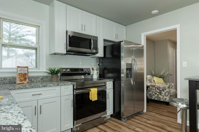 kitchen featuring decorative backsplash, appliances with stainless steel finishes, light stone counters, light hardwood / wood-style floors, and white cabinetry