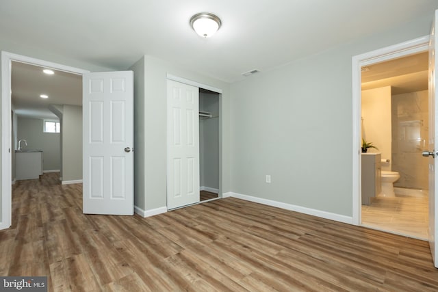 unfurnished bedroom featuring hardwood / wood-style floors, connected bathroom, and a closet