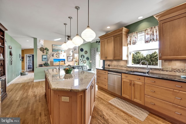 kitchen with sink, light hardwood / wood-style floors, stainless steel dishwasher, and an island with sink