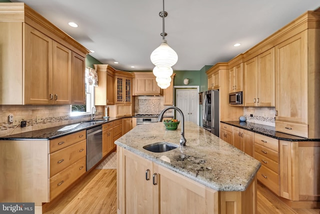 kitchen with sink, decorative light fixtures, light stone counters, and an island with sink