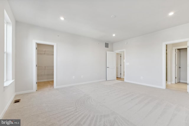 unfurnished bedroom featuring light colored carpet, a walk in closet, and a closet