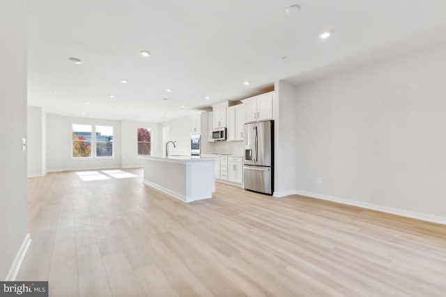 kitchen featuring white cabinetry, sink, a kitchen island with sink, appliances with stainless steel finishes, and light wood-type flooring