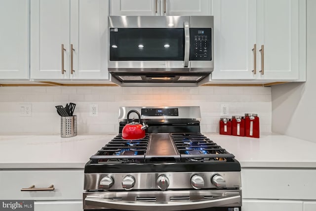 kitchen with light stone countertops, backsplash, white cabinetry, and stainless steel appliances