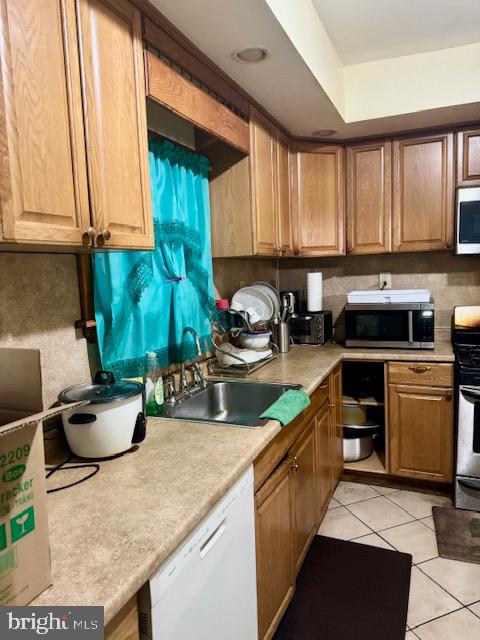 kitchen featuring backsplash, white dishwasher, sink, black range, and light tile patterned flooring