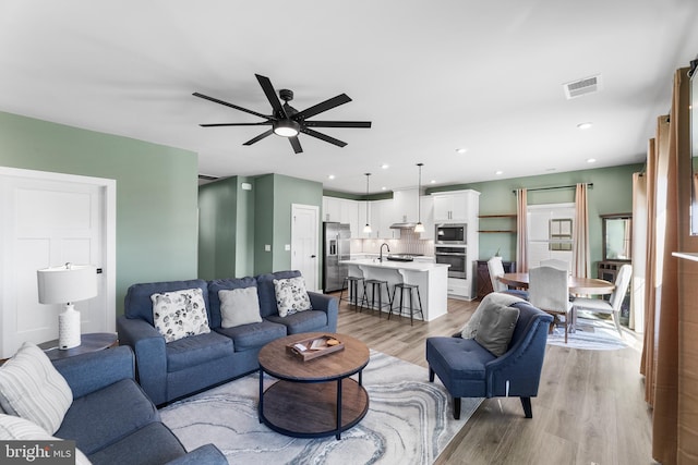 living room featuring ceiling fan, light wood-type flooring, and sink