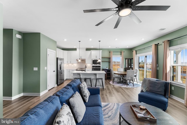 living room featuring ceiling fan, sink, and light wood-type flooring