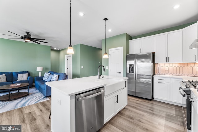 kitchen featuring white cabinets, appliances with stainless steel finishes, a center island with sink, and decorative light fixtures